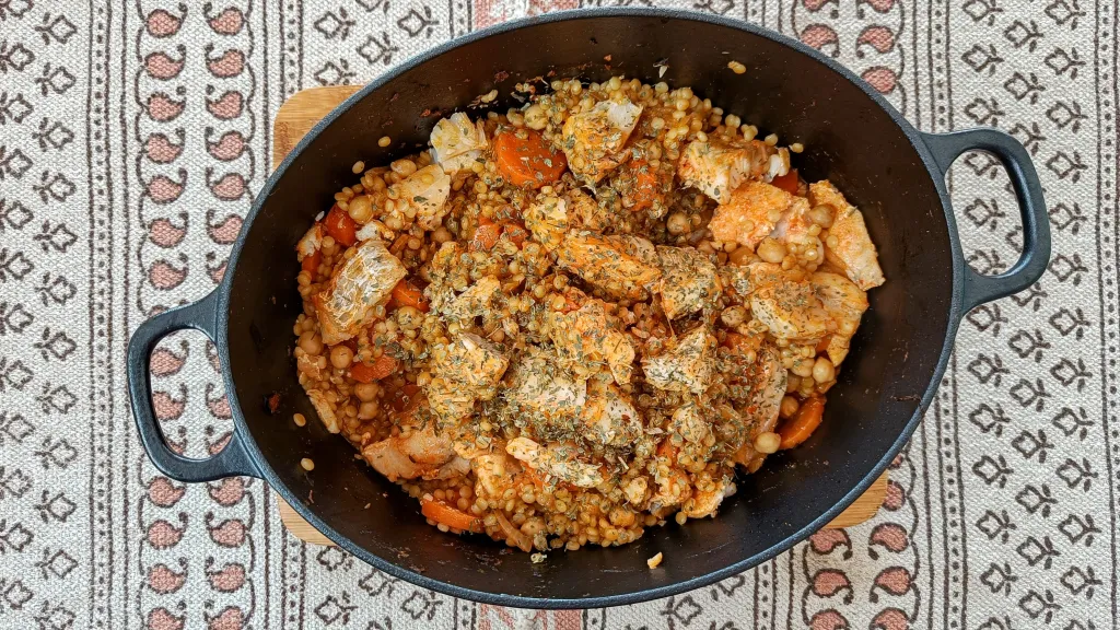 Photograph of Harissa baked cod with giant couscous, black chickpeas, carrots, coriander & lemon.
