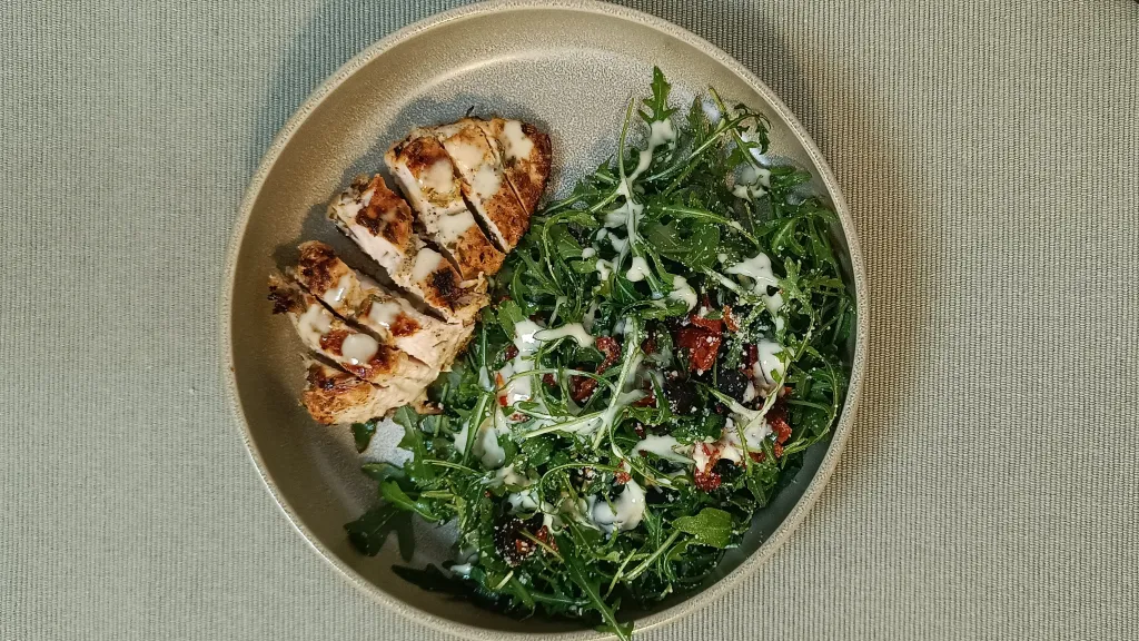 Photograph of Herby grilled chicken with rocket, sundried tomato and olive salad.