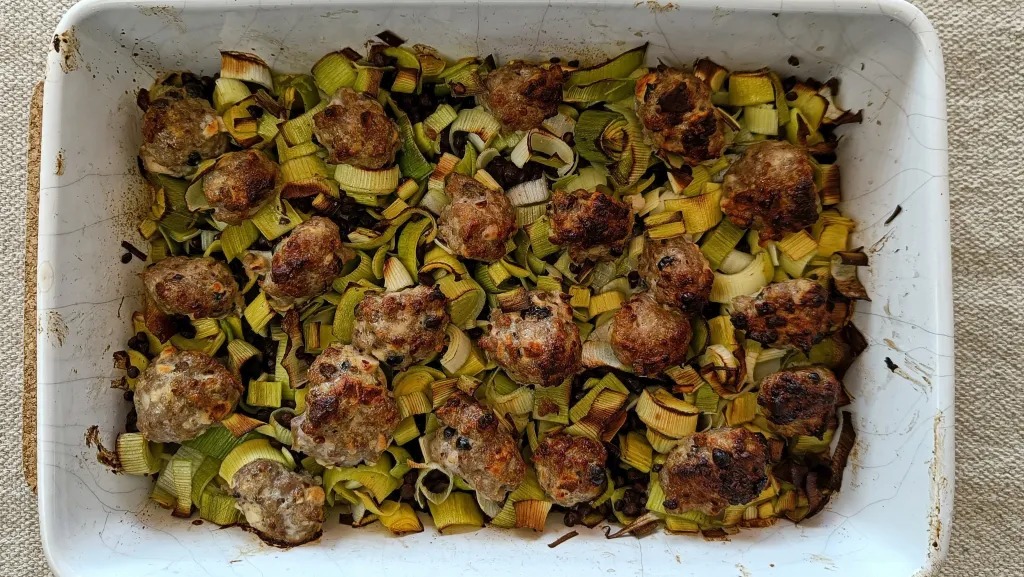 Photograph of Pork, juniper & pink peppercorn meatballs with leeks & puy lentils.