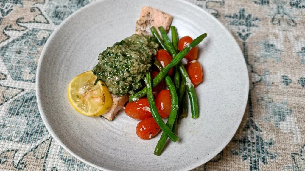 Photograph of Salmon fillets with vine tomatoes, beans and green sauce.